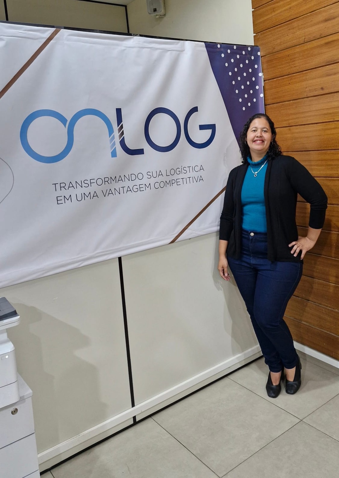 Priscilla Bento sorrindo em frente ao banner da Onlog